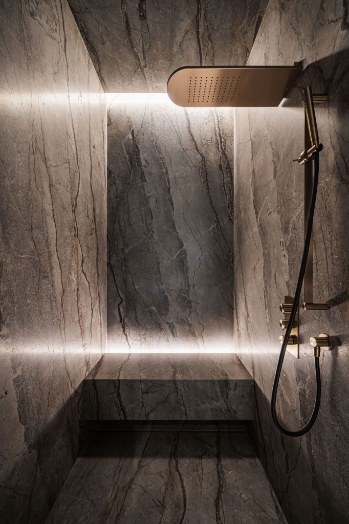 Full marble shower with minimal cove lighting and brass fixtures, designed by YODEZEEN