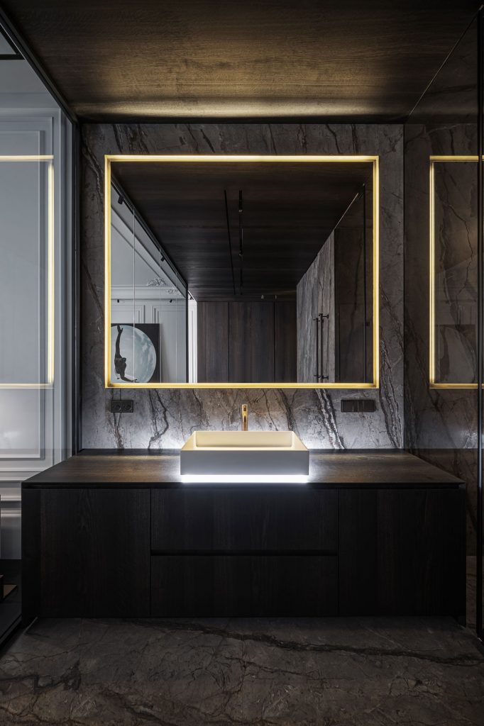 Master bathroom with dark grey marble walls with large square light framed mirror, dark wood block vanity and under-lit sink by YODEZEEN studio.