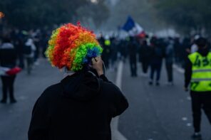 Protester in rainbow wig at Paris protest with crowd and French flag in background