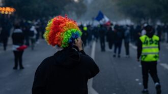 Protester in rainbow wig at Paris protest with crowd and French flag in background