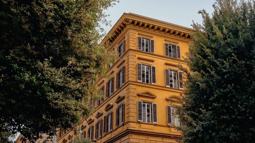 Experimental Roma building with ochre facade and classic shutters seen through trees
