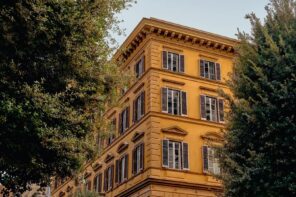 Experimental Roma building with ochre facade and classic shutters seen through trees