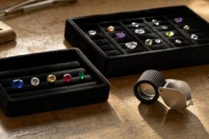 Loose gemstones in black trays and a jeweler's loupe on a wooden table