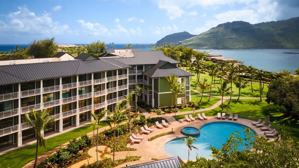 Hale Hōkūala Kauaʻi resort with pool, palm trees, and ocean in the background