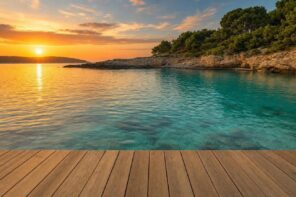 Wooden deck facing a tranquil bay at sunset with rocky shore and trees